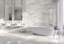 Płytka gresowa, podłogowa w kolorze szarym imitująca beton, wykończenie powierzchni polerowane, Cerrad Masterstone White Poler 59,7x59,7 położona na ścianie i podłodze w łazience gdzie znajduje się duża wanna oraz dwie umywalki i dwa lustra