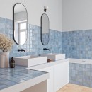 Płytka ścienna, dekoracyjna w kolorze niebieskim, wykończenie powierzchni w połysku, Gayafores Deco Amaris Blue 32x62,5 położona na ścianie w łazience gdzie znajdują się dwie umywali oraz dwa wiszące lustra