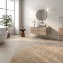 Płytka gresowa, podłogowa imitująca kamień w kolorze kremowym, wykończenie powierzchni satynowe, Pamesa Hermes Cream Satyna 60x120 położona na ścianie w łazience gdzie znajduje się biała wanna, wisząca szafka z umywalką a nad nią okrągłe lustro