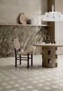 Gresowa podłogowa płytka imitująca beton Fioranese The Blend Concrete Sand Naturale 90,6x90,6 GC902R na ścianie nowoczesnej jadalni w połączeniu z ponadczasowym drewnem oraz oryginalnym wiklinowym krzesłem