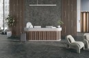 Płytka gresowa, podłogowa imitująca kamień w kolorze grafitowym, wykończenie powierzchni matowe,Rocersa Highlands Dark 60x120 położona na podłodze i ścianie w pomieszczeniu gdzie znajdują się jasne fotele, recepcja oraz ozdobne rośliny