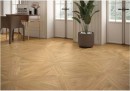 Gresowa podłogowa płytka imitująca drewno Oset Ceramiche Versalles Honey 100x100 na podłodze salonu w zestawieniu z drewnianym stolikiem, białą boazerią na ścianach oraz czarnymi elementami dekoracyjnymi na przeszklonych drzwiach