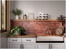 Gresowa płytka cegiełka w brązowym kolorze Oset Ceramiche Menorca Terra 5x50 na ścianie kuchni w połączeniu z białą  płytką, białymi meblami oraz drewnianym blatem
