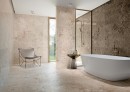 Gresowa podłogowa płytka imitująca kamień Grespania Artic Beige Mat 60x120 na ścianach i podłodze łazienki z kabiną prysznicową w czarnej ramie, wanną wolnostojącą i złotą armaturą łazienkową