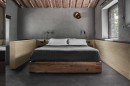 Sypialnia w klimacie loftowym, gdzie na podłodze zastosowano ciemnoszare, strukturalne płytki Marazzi Mystone Pietra Ligure Antracite Strutturato, imitujące kamień, centralnie umieszczone łóżko otoczone jest jasnymi panelami ściennymi