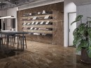 Płytka gresowa, podłogowa imitująca metal, wykończenie powierzchni w połysku, Fanal Planet Oxide Metal Shine Rect. 60x120 położona na na podłodze oraz ścianie w pomieszczeniu gdzie znajduje się ciemny stół z krzesłami, wisząca lampa oraz roślina ozdobna