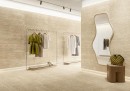 Gresowa podłogowa płytka imitująca kamień trawertyn w beżowym kolorze Fioranese Senzatempo Beige Naturale 75x149,7 TT712R na ścianach i podłodze salonu mody w zestawieniu ze złotymi wieszakami, lustrem w złotej ramie i drewnianym postumentem
