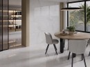 Płytka gresowa w kolorze szarym imitująca metal, wykończenie powierzchni w połysku, Fanal Planet White Metal Shine Rect. 60x120 położona na podłodze oraz ścianie w pomieszczeniu gdzie znajduje się drewniany stół oraz krzesła, duże okno z widokiem na ogród