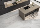 Płytka gresowa, podłogowa imitująca marmur w szarym kolorze, wykończenie powierzchni satynowe, Pamesa Apulia Gold Satin 60x60 położona na podłodze w kuchni gdzie znajduje się ciemna kuchenna zabudowa, wyspa oraz ciemne krzesełka