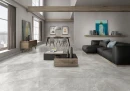 Płytka gresowa, podłogowa imitująca kamień w szarym kolorze, wykończenie powierzchni satynowe, Pamesa Arezzo Perla Satin 60x120 położona w salonie na podłodze gdzie znajduje się ciemny wypoczynek, stolik kawowy oraz stół jadalny