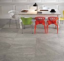 Gresowa podłogowa płytka imitująca szary kamień Saime Artica Nube Lappato 60x60 8600370 wyłożona w biurze na podłodze. Biała sztukateria na ścianie. Klasyczny prostokątny stół z rzeźbionymi nogami. Kolorowe nowoczesne krzesła.