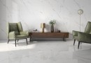 Płytka gresowa, podłogowa imitująca marmur w białym kolorze, wykończenie powierzchni w połysku, Pamesa Castello Oro Polished 120x120 położona na ścianie i podłodze w salonie gdzie znajduje się drewniana szafka oraz dwa zielone fotele