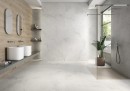 Płytka gresowa, podłogowa imitująca kamień w białym kolorze, wykończenie powierzchni w połysku, Pamesa Creta White Polished 60x60 położona na podłodze i ścianie w łazience gdzie znajduje się prysznic, dwie białe umywalki oraz wiszące lustra