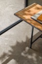 Bliskie ujęcie podłogi wyłożonej beżowymi płytkami gresowymi Marazzi Mystone Pietra Ligure Beige Strutturato 60x120 cm MPK3, imitującymi kamień, w tle widoczny narożnik stolika kawowego z metalową ramą i blatem w ciepłym, rdzawym odcieniu