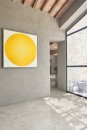 Nowoczesne wnętrze z dużą ilością światła, gdzie na podłodze zastosowano płytki gresowe Marazzi Mystone Pietra Ligure Bianco 60x60 cm MPK7 imitujące jasny kamień, na ścianie z surowego tynku wisi obraz przedstawiający duży, jaskrawożółty okrąg