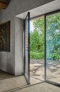Wnętrze z nowoczesnymi, przeszklonymi drzwiami prowadzącymi na zewnątrz, gdzie na podłodze zastosowano beżowe płytki gresowe Marazzi Mystone Pietra Ligure Beige R10 60x60 cm MPKA, imitujące kamień, na ścianie z surowego tynku po lewej stronie wisi obraz