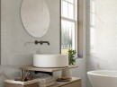 Płytka gresowa, podłogowa imitująca kamień w białym kolorze, wykończenie powierzchni satynowe, Pamesa Onix White Satin 60x120 położona na ścianie w łazience gdzie znajduje się półka z białą umywalką, wiszące lustro oraz okno z widokiem na ogródek