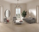 Gresowa podłogowa płytka imitująca beżowy kamień Saime Avalon Blanc Grip 60x60 8690102 na podłodze dużego przestronnego salonu. Szare fotele i kanapa. Marmurowy okrągły stolik z czarnymi nogami.