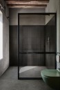 Nowoczesna łazienka w surowym stylu, z podłogą wyłożoną ciemnymi, antypoślizgowymi płytkami gresowymi Marazzi Mystone Pietra Ligure Antracite R10 60x60 cm MPKE, widoczna jest kabina prysznicowa z czarną ramą oraz ściany z szorstkiego tynku