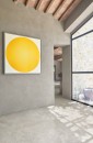 Jasna, rustykalna przestrzeń wyłożona wielkoformatowymi płytkami gresowymi Marazzi Mystone Pietra Ligure Bianco 75x150 cm MPKF, imitującymi kamień w odcieniu złamanej bieli, na ścianie z surowego tynku wisi obraz przedstawiający duży, jaskrawożółty okrąg