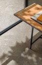 Bliskie ujęcie podłogi wyłożonej wielkoformatowymi beżowymi płytkami gresowymi Marazzi Mystone Pietra Ligure Beige 75×150 MPKG, imitującymi kamień o ciepłym odcieniu, na podłogę pada cień liści, a w kadrze znajduje się metalowy stolik