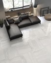 Płytka gresowa, podłogowa imitująca kamień w białym kolorze, wykończenie powierzchni satynowe, Pamesa Whitehall Blanco Satin 60x60 położona na podłodze  w salonie gdzie znajduje się ciemny wypoczynek, półka z książkami oraz duże okno