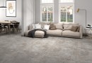 Płytka gresowa, podłogowa imitująca beton w szarym kolorze, wykończenie powierzchni matowe, Pamesa Argile Opal Matt 60x60 położona na podłodze w salonie gdzie znajduje jasny wypoczynek, stół z krzesłami oraz okno z widokiem na miasto