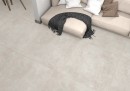 Płytka gresowa, podłogowa imitująca beton w kolorze szarym, wykończenie powierzchni matowe, Pamesa Argile Chalk Matt 120x120 położona na podłodze w pomieszczeniu gdzie znajduje się beżowa kanapa