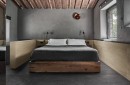Sypialnia w nowoczesnym stylu rustykalnym ma podłogę wyłożoną ciemnymi płytkami gresowymi Marazzi Mystone Pietra Ligure Antracite 75x75 cm MPKK, imitującymi kamień, wnętrze to charakteryzują surowe, szare ściany oraz odsłonięte drewniane belki sufitowe