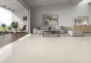 Płytka gresowa, podłogowa imitująca beton w beżowym kolorze, wykończenie powierzchni matowe, Pamesa Coralstone Marfil Antic 90x90 położona na podłodze w salonie gdzie znajduje się jasny wypoczynek, stolik oraz drewniana szafka