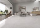 Płytka gresowa, podłogowa imitująca beton w szarym kolorze, wykończenie powierzchni matowe, Pamesa Coralstone Perla Antic 90x90 położona na podłodze w salonie gdzie znajduje się jasny wypoczynek, stolik oraz drewniana szafka