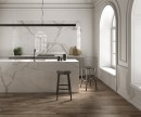 Gresowa podłogowa płytka imitująca marmur z szarą żyłą Saime Cave Pietrasanta Naturale 60x120-6mm T810305 na ścianie i wyspie kuchennej. Ciemna drewniana płytka na podłodze. Duże okna w białej ramie ze szprosami. Biała sztukateria na na ścianach.