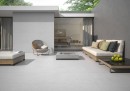 Płytka gresowa, podłogowa imitująca beton w szarym kolorze, wykończenie powierzchni matowe, Pamesa Cromat Blanco Matt 60x60 położona na tarasie gdzie znajduje się wypoczynek, stolik oraz wejście do domu
