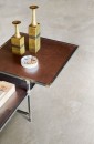 Bliskie ujęcie wnętrza z podłogą wyłożoną jasnymi płytkami gresowymi Marazzi Mystone Pietra Ligure Bianco 75×75 cm MPKN, imitującymi kamień, na metalowym stoliku z miedzianym blatem stoją dwie mosiężne wazy