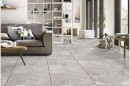 Płytka gresowa, podłogowa lastryko w szarym kolorze, wykończenie powierzchni matowe, Netto Ceramika Terazzo Grey Luster Matt 60x120 położona na podłodze w salonie gdzie znajduje się kanapa, stolik, oraz okna z widokiem na ogród