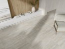 Płytka gresowa, podłogowa imitująca kamień w beżowym kolorze, wykończenie powierzchni matowe, Pamesa Dorset Gris Matt 120x120 położona na podłodze gdzie znajduje się jasny fotel oraz półka