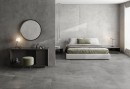 Płytka gresowa, podłogowa imitująca beton w szarym kolorze, wykończenie powierzchni matowe, Pamesa Eleganza Gris Matt 60x120 położona na ścianie oraz podłodze w sypialni gdzie znajduje się łóżko, lampy oraz tolaetka