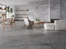 Kamienna płytka gresowa imitująca szary kamień Pamesa Erding Silver Matt 30x60 położona na ścianie salonu z kominkiem, wypoczynkiem oraz drewnianym stołem