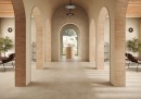 Przestronny hol z podłogą wyłożoną beżowymi płytkami Marazzi Mystone Tivoli Beige 160x160 cm MQAC, symetryczne łuki i kolumnady nadają wnętrzu klasyczny, śródziemnomorski charakter