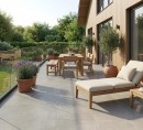 Płyta tarasowa imitująca beton w beżowym kolorze, wykończenie powierzchni matowe, Pamesa Essen Ash Matt 60x60 - 20mm położona na tarasie przed domem gdzie znajduje się leżak, stół wraz z krzesłami oraz ozdoby roślinne