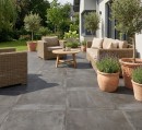Płyta tarasowa, gresowa imitująca beton w grafitowym kolorze, wykończenie powierzchni matowe, Pamesa Essen Zircon Matt 60x60 - 20mm położona na tarasie gdzie znajduje się wypoczynek, drewniany stolik oraz ozdobne rośliny