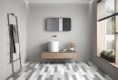 Płytka gresowa, podłogowa imitująca beton w szarym kolorze, wykończenie powierzchni matowe, Pamesa Essenza Beige Matt 60x120 położona na ścianie w łazience gdzie znajduje się szafka wisząca z umywalką, wiszące lustro, duże okno oraz wieszak na ręczniki