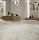 Wnętrze nowoczesnego butiku z drewnianymi półkami i szarymi płytkami podłogowymi imitującymi trawertyn  Caesar Iconica Silver Contro