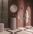 Mobilcrab Fount4 ceramiczna umywalka wolnostojąca okrągła w kolorze matowego różu w łazience gdzie znajduje się wiszące okrągłe lustro, oraz, pufa, prysznic raz wieszaki