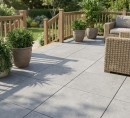 Płyta tarasowa, gresowa imitująca beton w szarym kolorze, wykończenie powierzchni matowe, Pamesa Koncept Argent 60x60 - 20mm położona na tarasie gdzie znajduje się wypoczynek, rośliny ozdobne oraz ogród