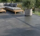 Płyta tarasowa, gresowa imitująca beton w grafitowym kolorze, wykończenie powierzchni matowe, Pamesa Koncept Mica 60x60 - 20mm położona na tarasie gdzie znajduje się wypoczynek, ozdobna roślina oraz widok na ogród