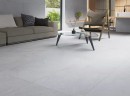 Płytka gresowa, podłogowa imitująca kamień w białym kolorze, wykończenie powierzchni satynowe, Keraben Verse White Soft 60x120 położona na podłodze w salonie gdzie znajduje się wypoczynek, szklany stolik oraz okno z widokiem na ogród
