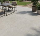 Płyta tarasowa, gresowa imitująca beton w szarym kolorze, wykończenie powierzchni matowe antypoślizgowe, Pamesa Mosel Sand Matt 60x60 - 20mm położona na tarasie gdzie znajduje się stół z krzesłami, oraz ogród