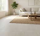 Płytka gresowa, podłogowa imitująca beton w szarym kolorze, wykończenie powierzchni matowe, Pamesa Mosel Ash Matt 90x90 położona na podłodze w salonie gdzie znajduje się jasna kanapa, drewniany stolik, dywan oraz duże okno