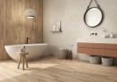Płytka gresowa, podłogowa imitująca kamień w beżowym kolorze, wykończenie powierzchni matowe, Pamesa Natural Sense Beige Matt 120x120 położona na ścianie w łazience gdzie znajduje się biała wanna, szafka z umywalka oraz wiszące lustro